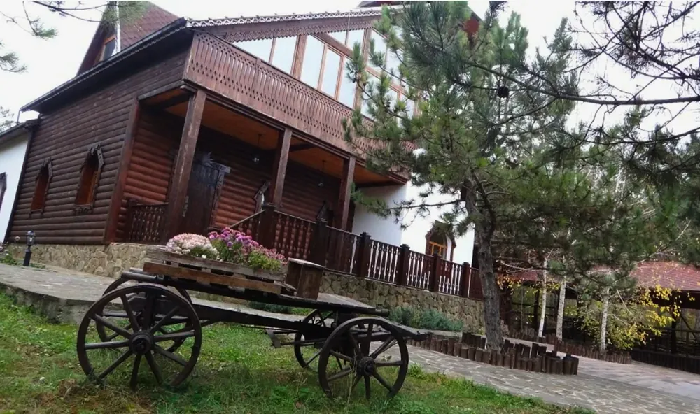 Деревянный дом площадки, перед ним старинная телега с цветами